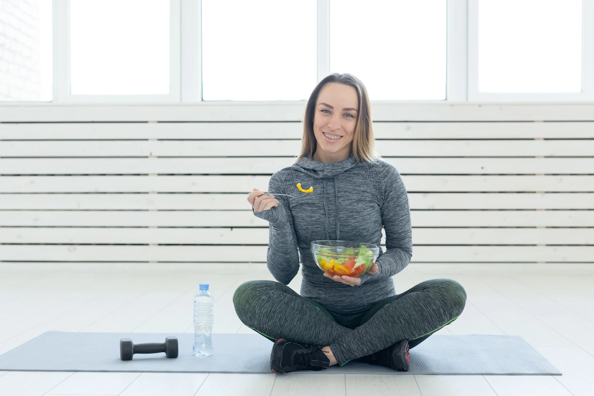 Une femme qui prend un bol de salade assis sur le sol